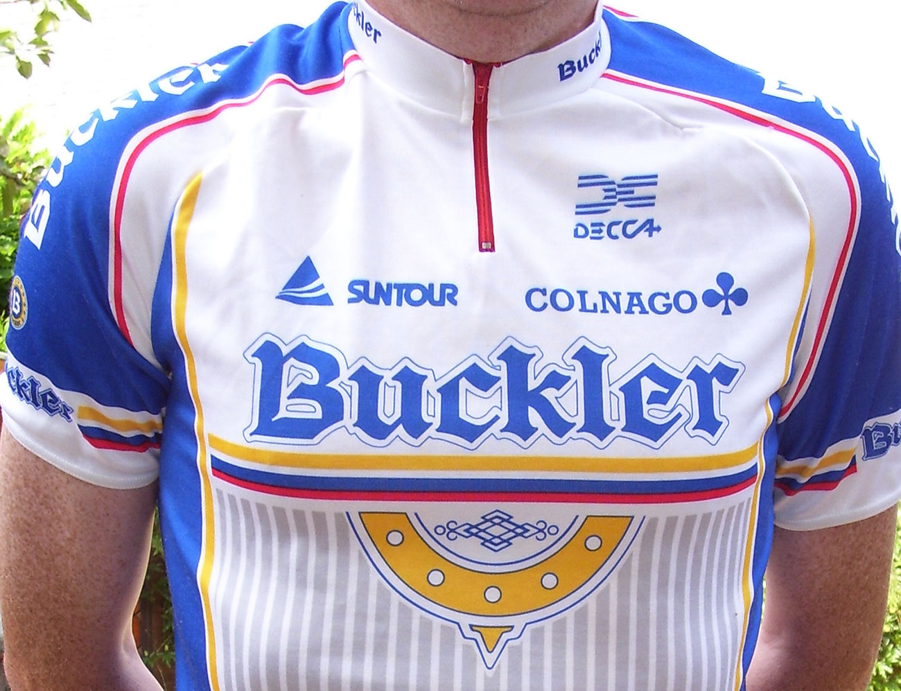 A cyclist wearing a shirt adorned with logos. Some are small and some are larger.